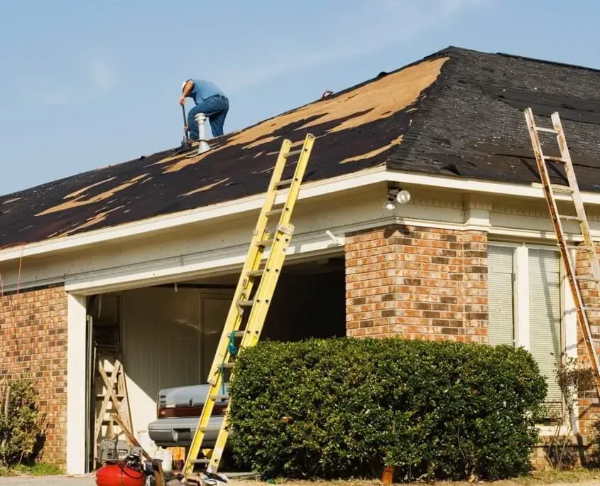 Home undergoing roof replacement with man on roof nailing down new shingles