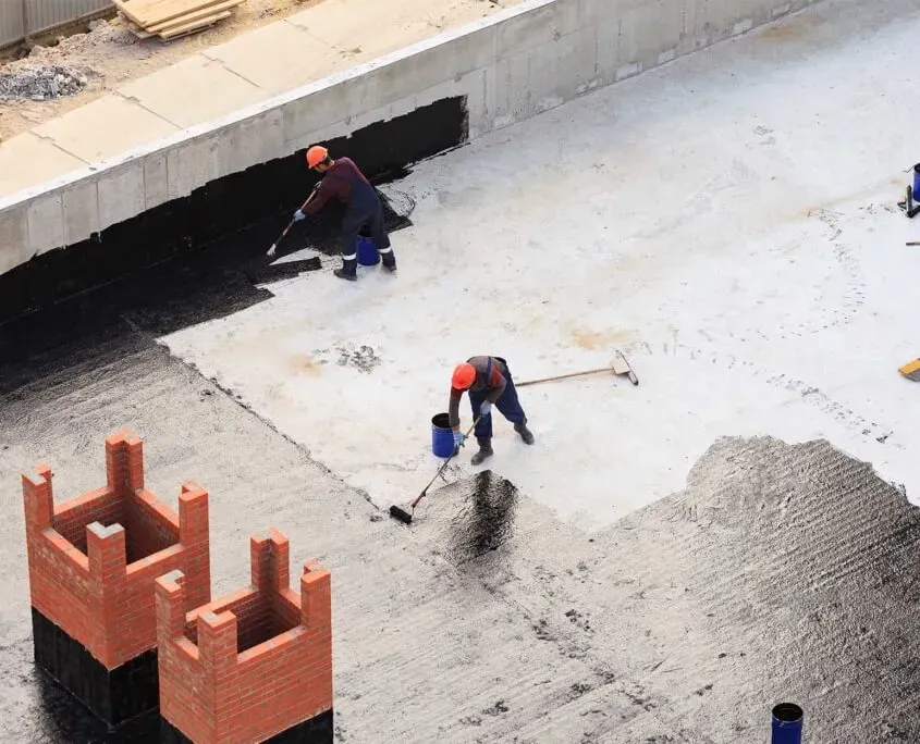 Image from above of men painting waterproofing substance onto commercial roof