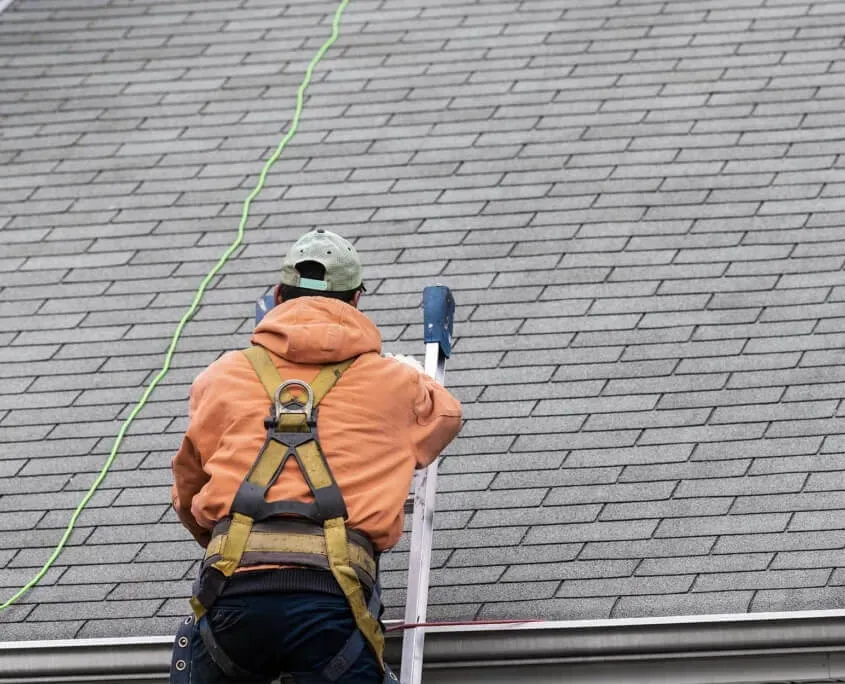Man on ladder leaned against residential roof inspecting damage