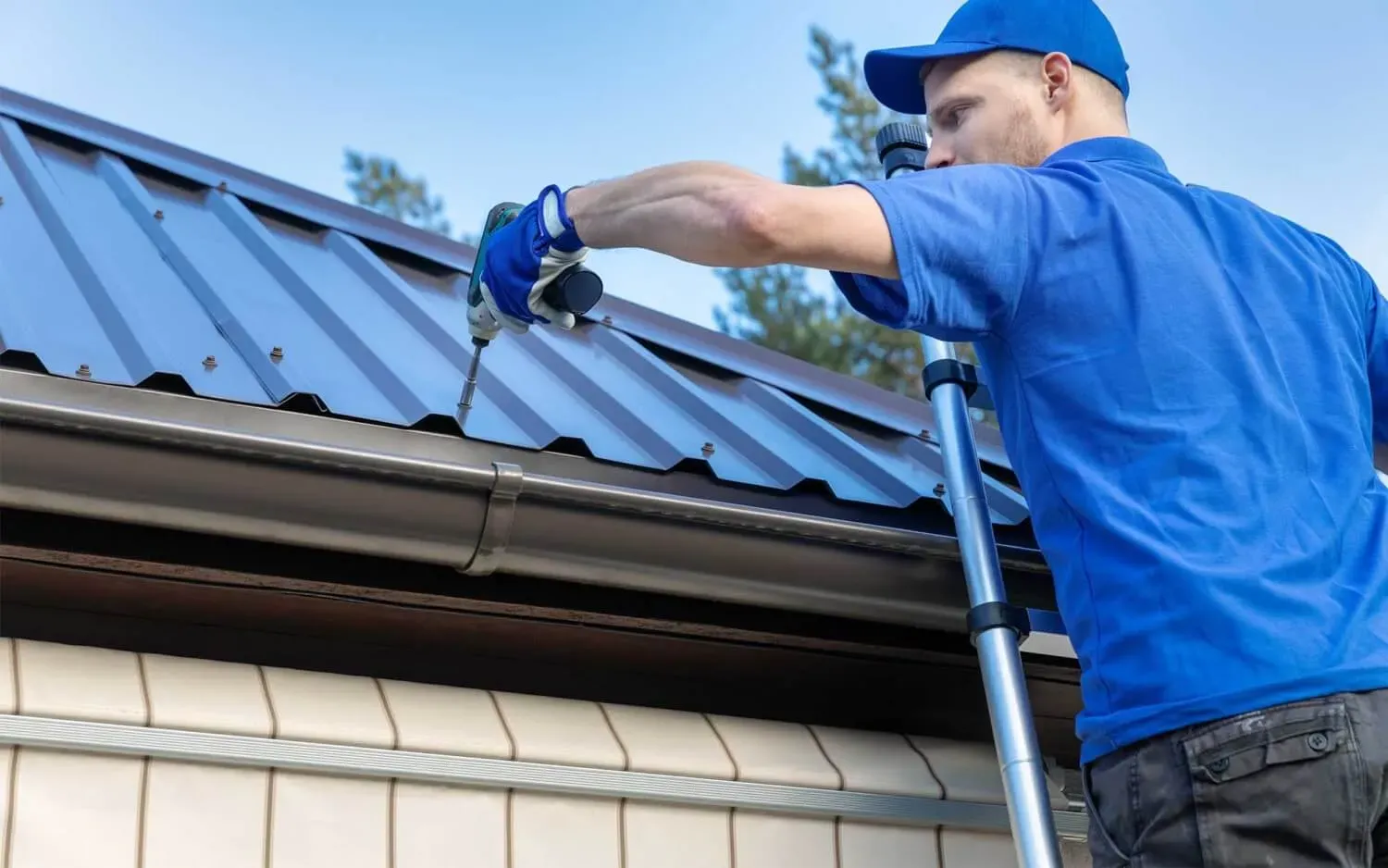 Man on ladder screwing in metal panel onto roof
