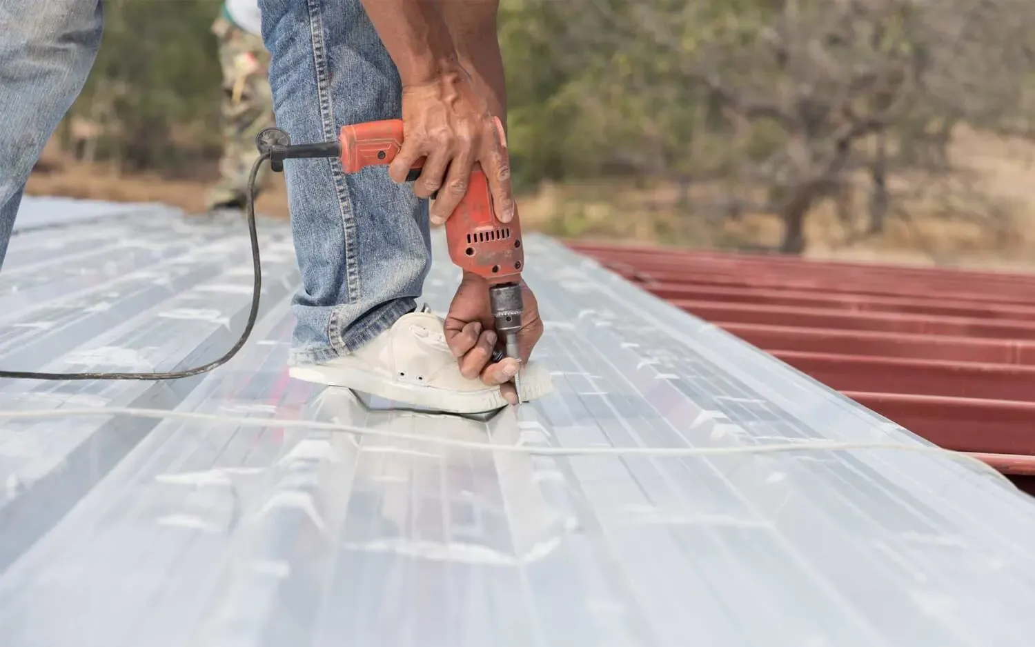 Man reaching down to screw in metal roof sheet