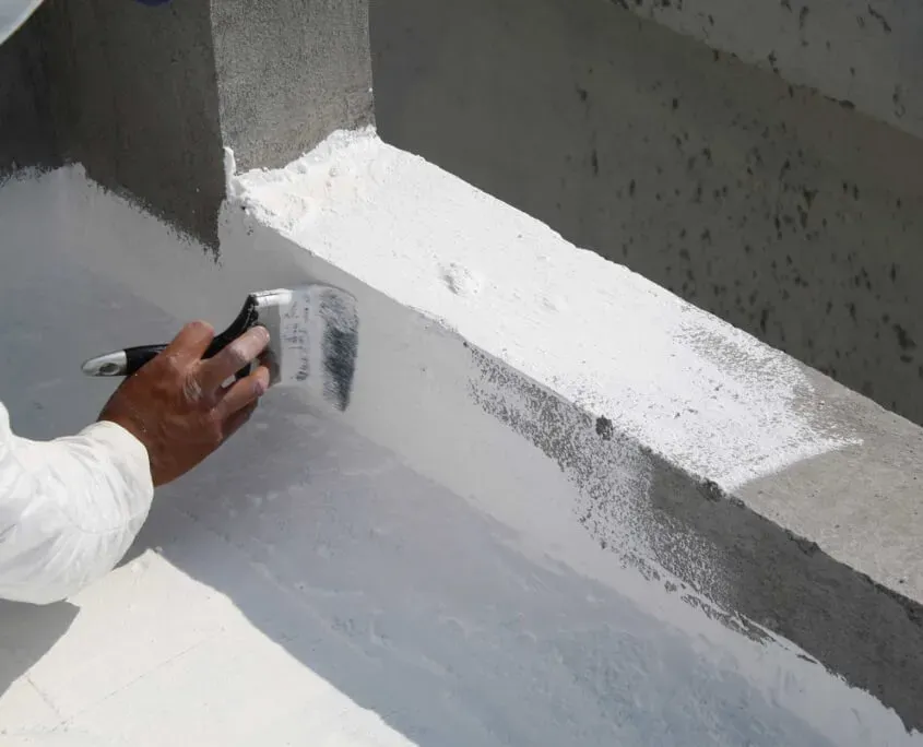 Man using paint brush to apply waterproofing substance to edges of a flat top commercial roof