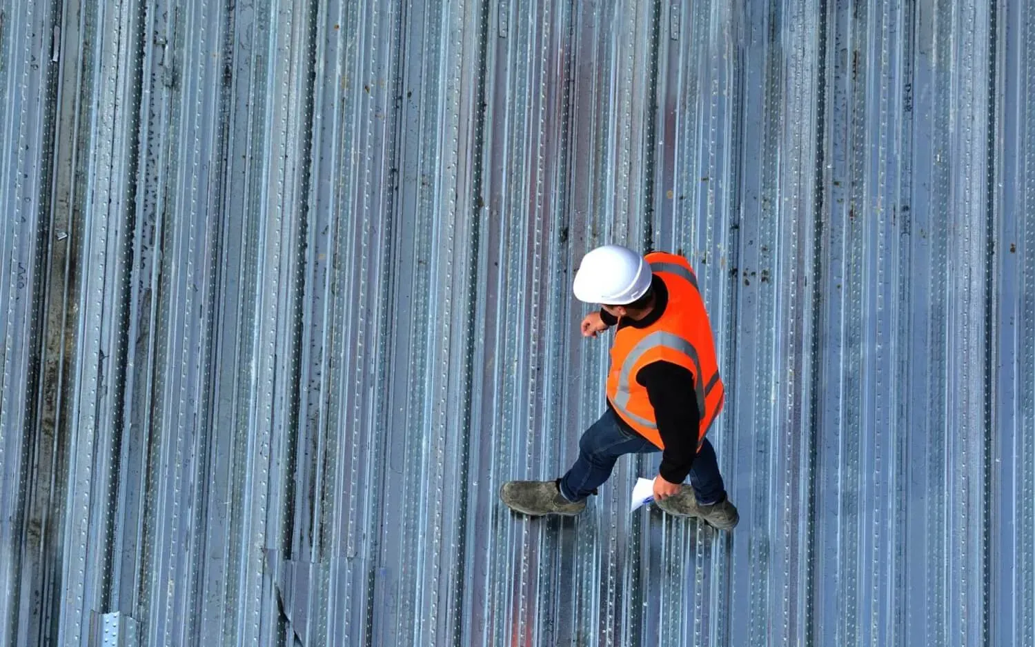 Man walking over metal roof conducting inspection
