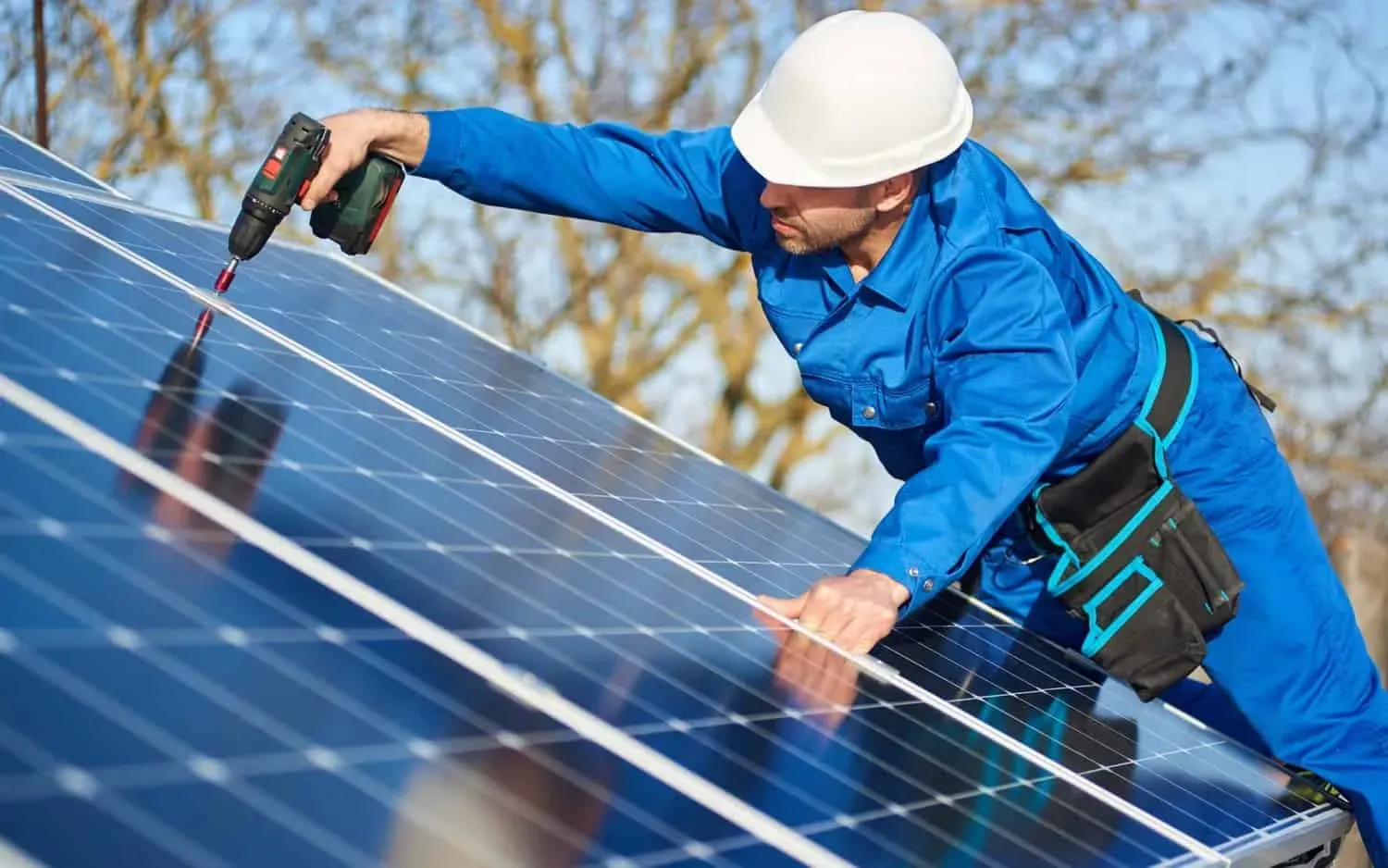 Man worker in blue suit and protective helmet installing solar photovoltaic panel system using screwdriver
